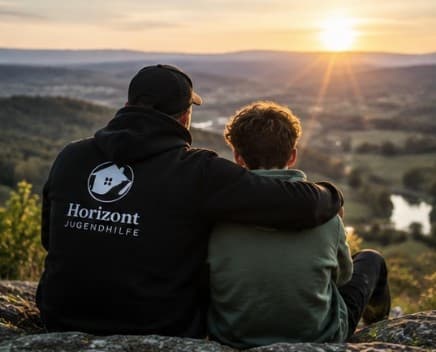 Pädagoge und Jugendlicher sitzen nebeneinander und blicken in den Sonnenuntergang