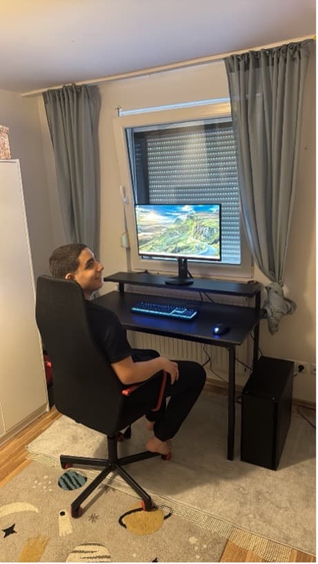 Jugendlicher sitzt am fertig aufgebauten Schreibtisch mit Monitor und Tastatur, dreht sich auf dem Bürostuhl zur Kamera
